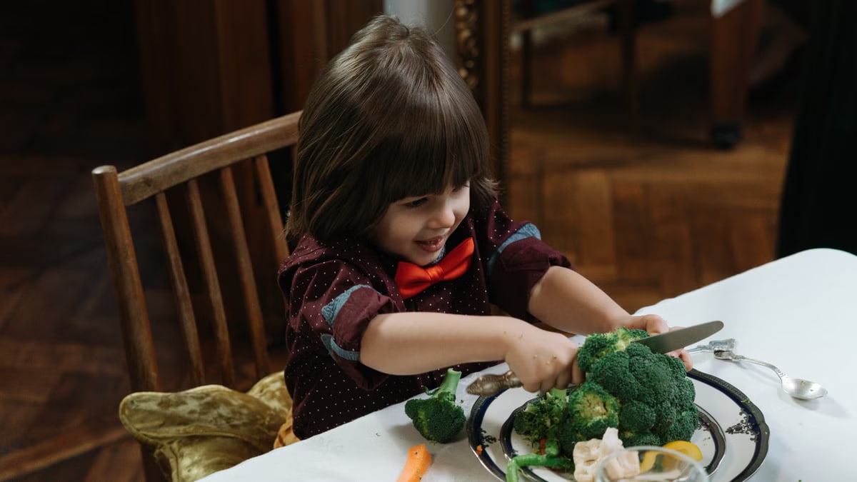 Young child excitedly cutting broccoli during a healthy meal at home.